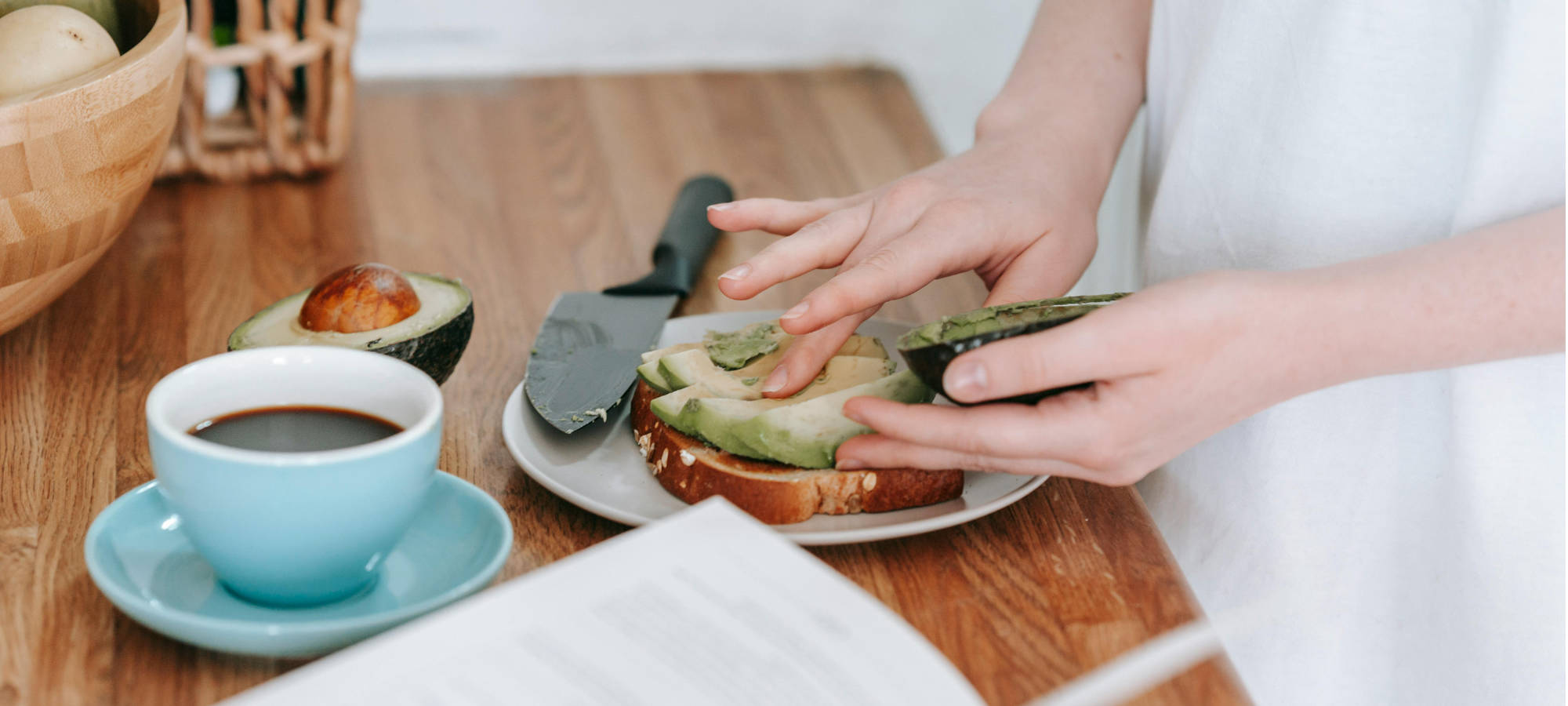 mani di donna che prepara toast con avocado accanto a tazza di caffe